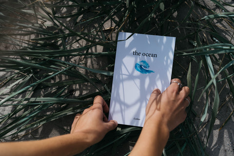 an image of hands holding "the ocean" poetry collection on a background of green grass