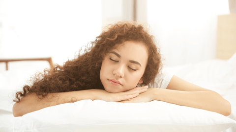 Woman with curly hair sleeping on hands with head on pillow