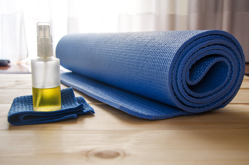 A picture of a rolled up yoga mat with cleaing spray next to i.
