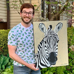Dorrin Gingerich holding his painting of Zebra 1. In front of a tree and some bushes.