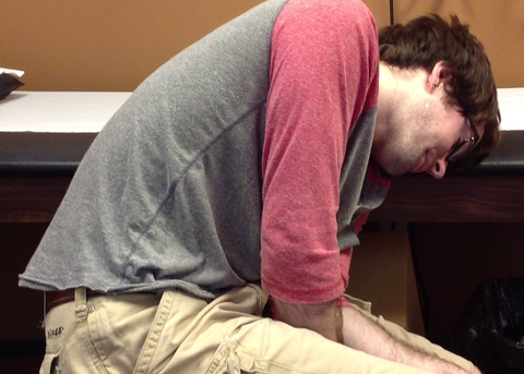 Dorrin Gingerich struggling with Dystonia at Doctors office, Resting his head on a table as his body shakes