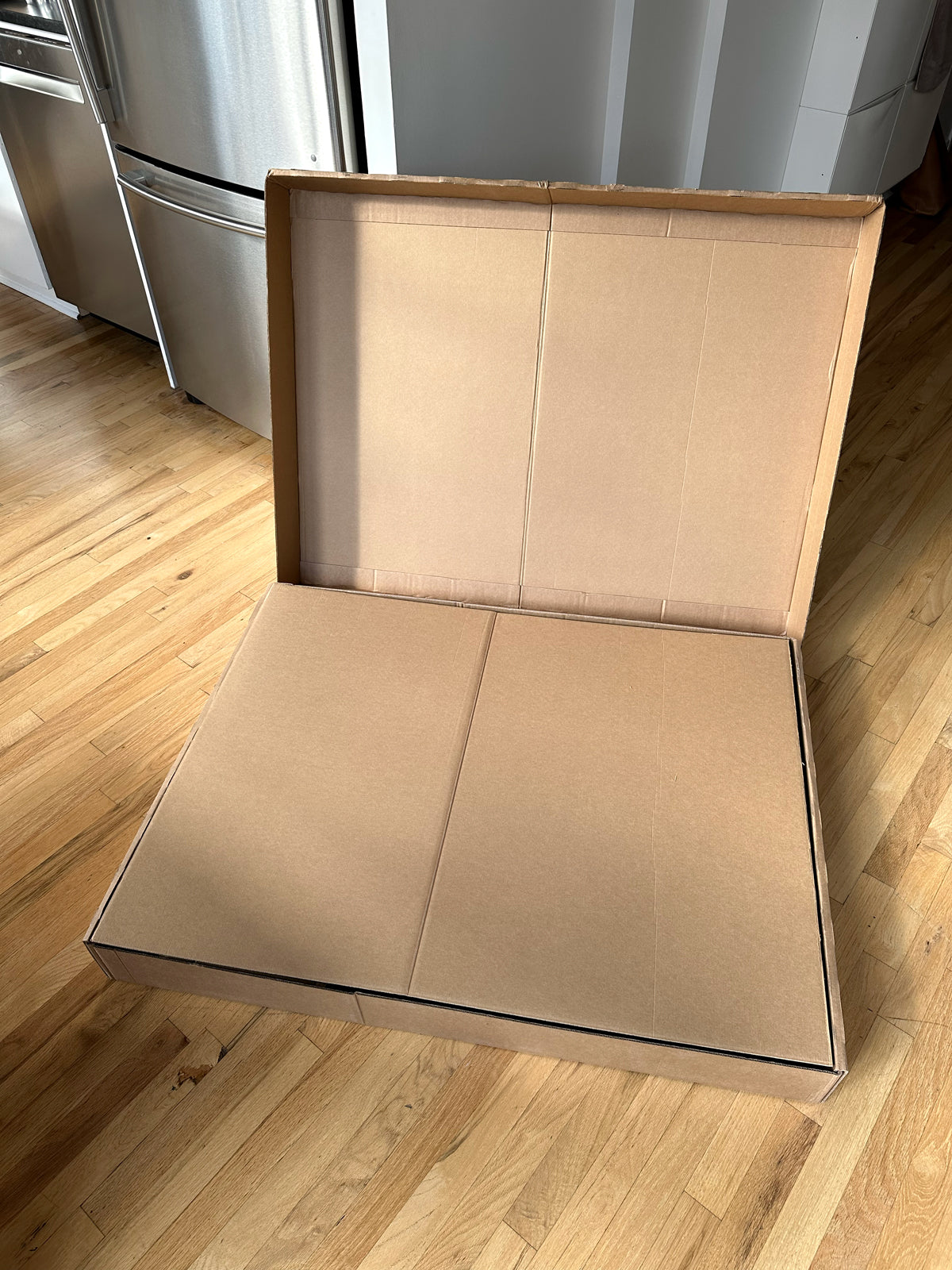 A cardbard box on the ground with the cover open showing another piece of cardboard as the top layer.