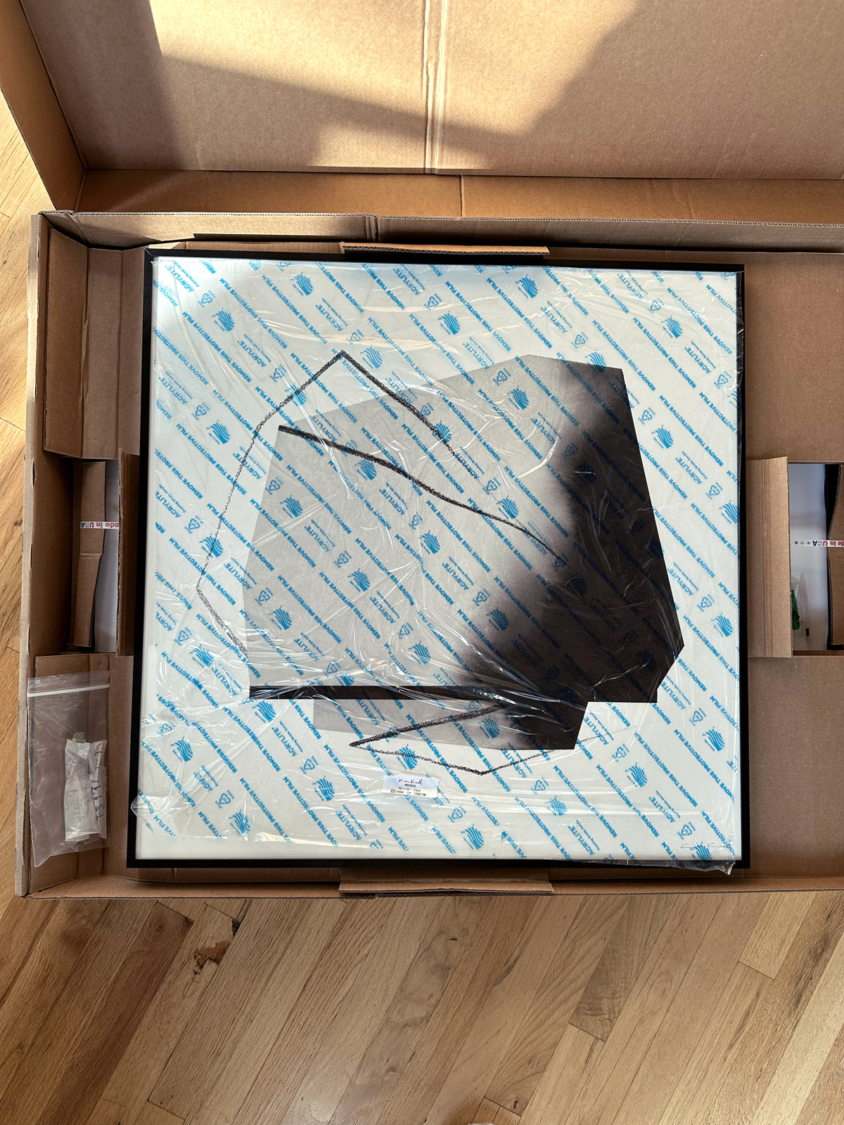 The front of an abstract artwork with protective plastic inside of a box