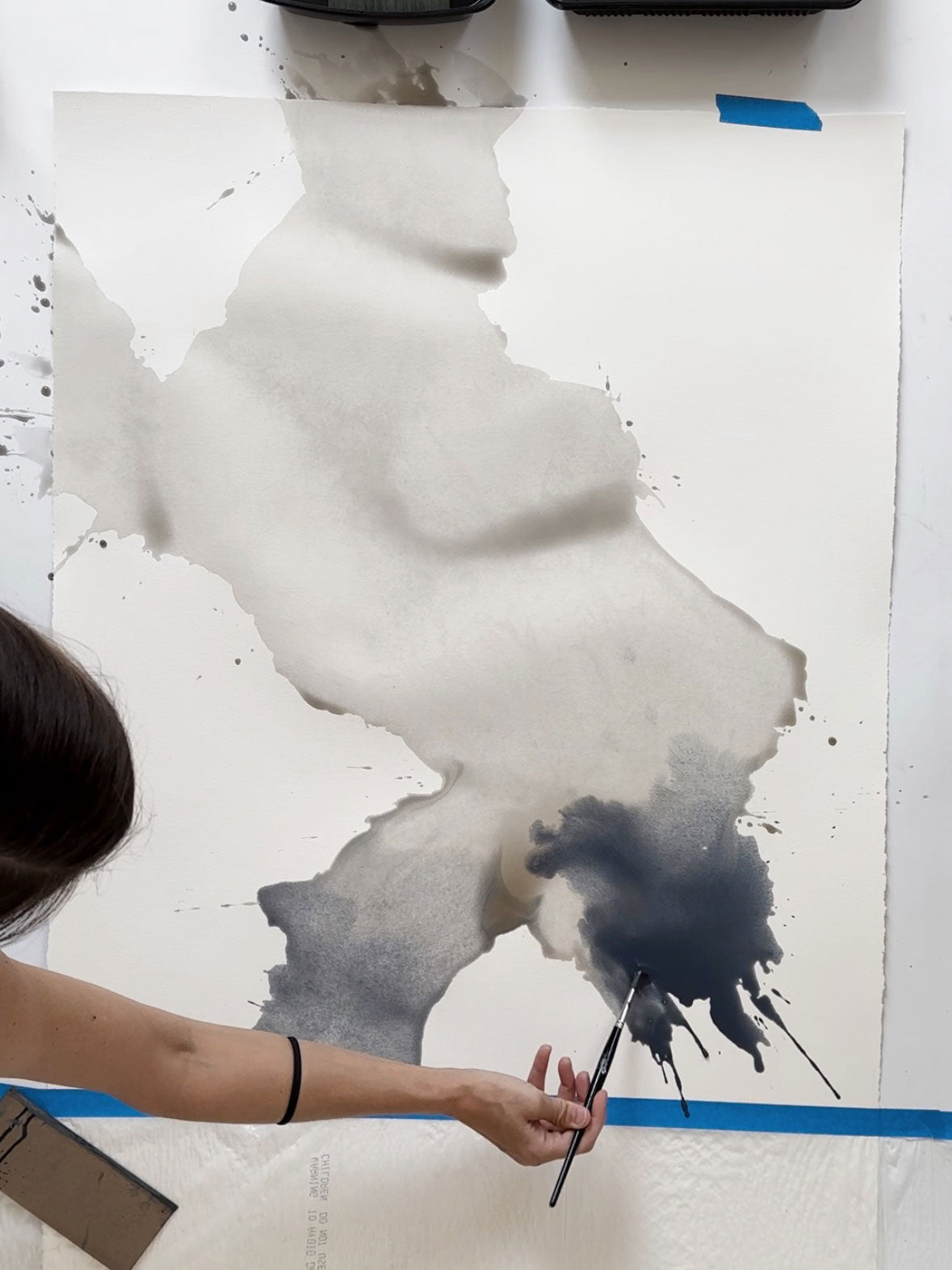 An organic splash of gray and blue watery paint being applied to paper