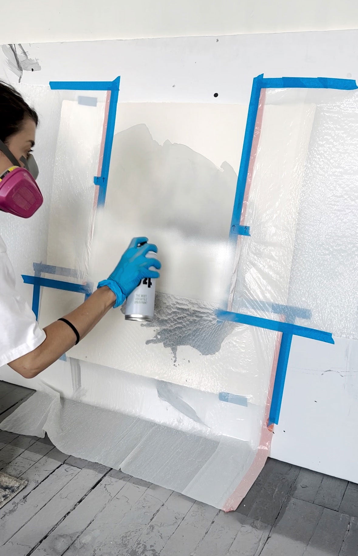 Kim spray painting a layer of white onto a painting