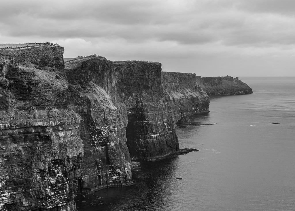ic:Shadows and Silhouettes: The Cliffs of Moher enshrouded in mystery and drama, as overcast skies cast their moody hues over the rugged Irish coastline.