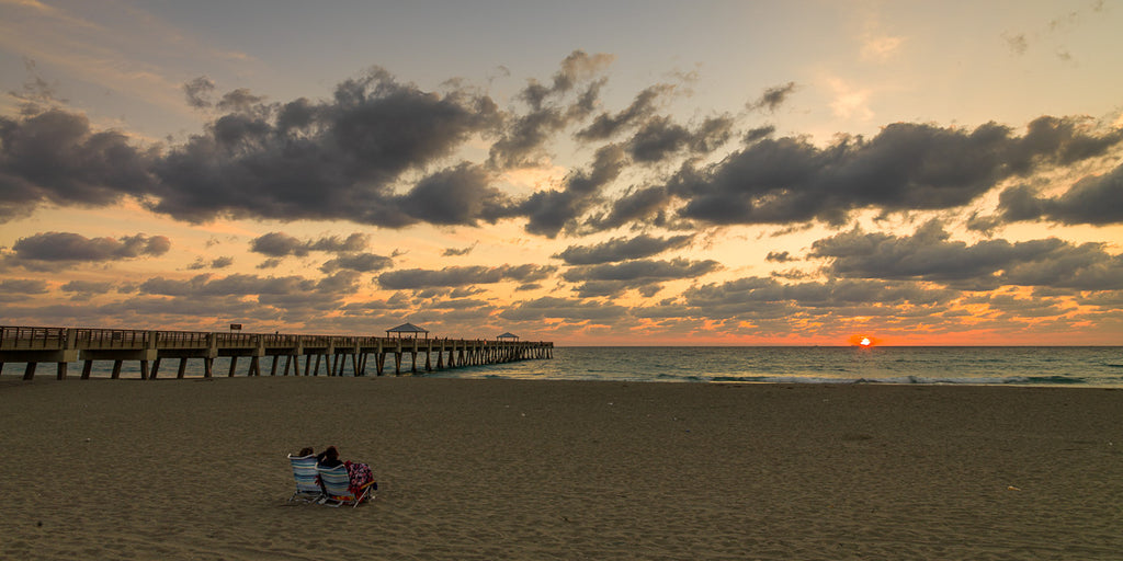 ic: Tranquil sunrise on the coast of Florida with a couple sitting enjoying the view