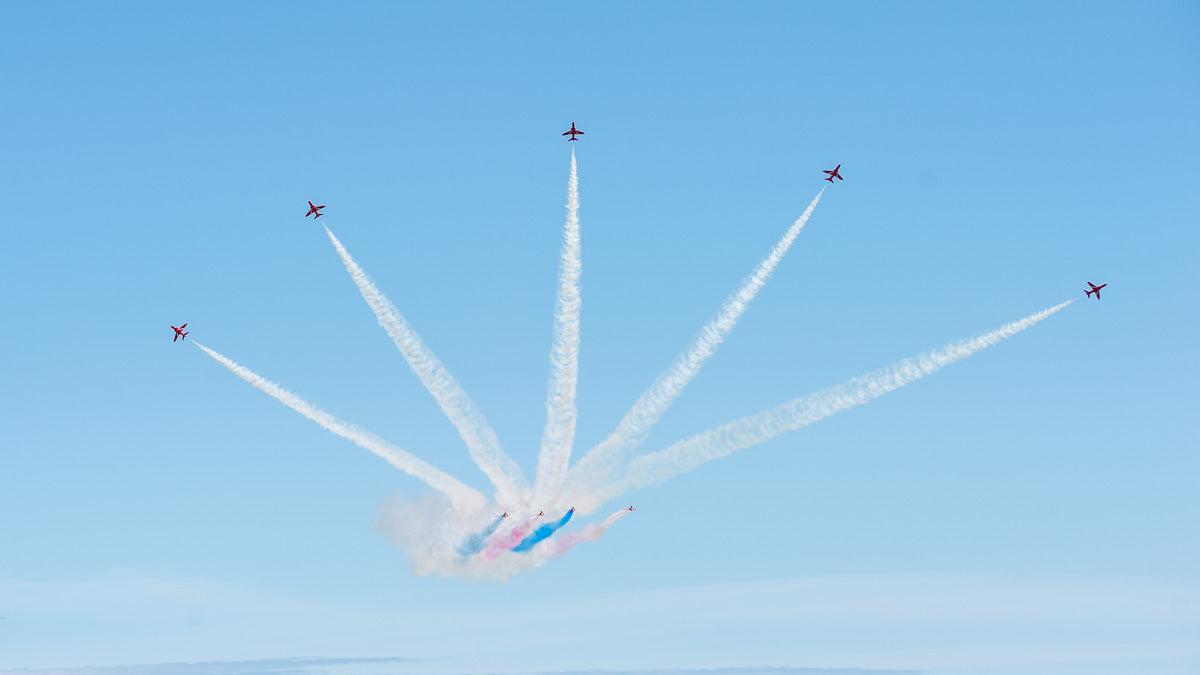 Red Arrows aerial display team against a blue sky with coloured jet streams