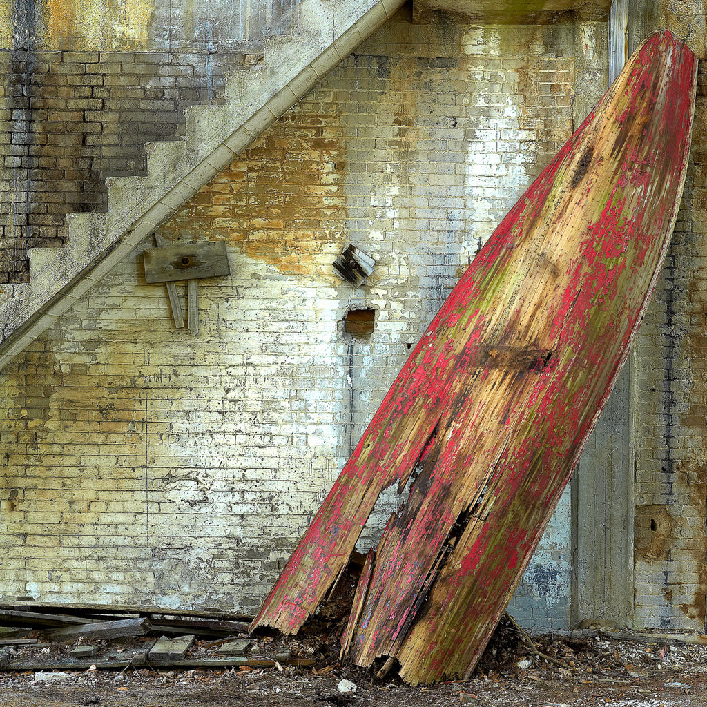 ic:An arresting juxtaposition of color and decay, this image captures a lone red rowboat resting against a crumbling wall, evoking a sense of stillness and abandonment amidst the relentless march of time.