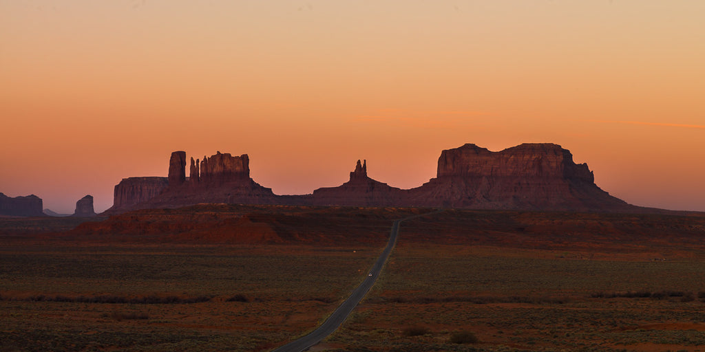 ic:The road to Monument Valley, bathed in the ethereal light of sunrise, promises a journey into the heart of the mystical American Southwest.