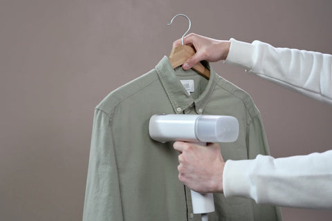Person holding a green button down while steaming the shirt