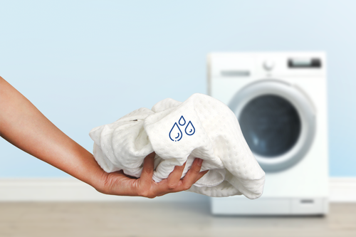 Hand holding white laundry with a washing machine in the background.