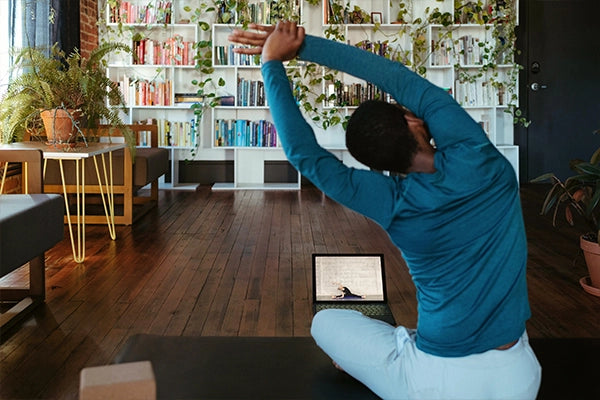 Person in blue exercise gear sitting on yoga mat stretching arms to the left