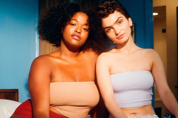 Two women sitting next to each other on bed in strapless crop tops