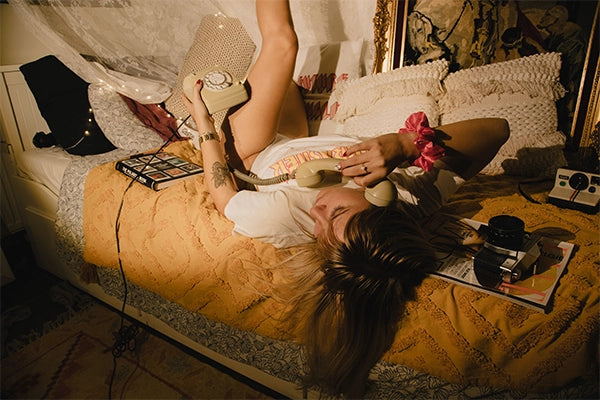 Girl in T-shirt and underwear lying on bed on back on phone call