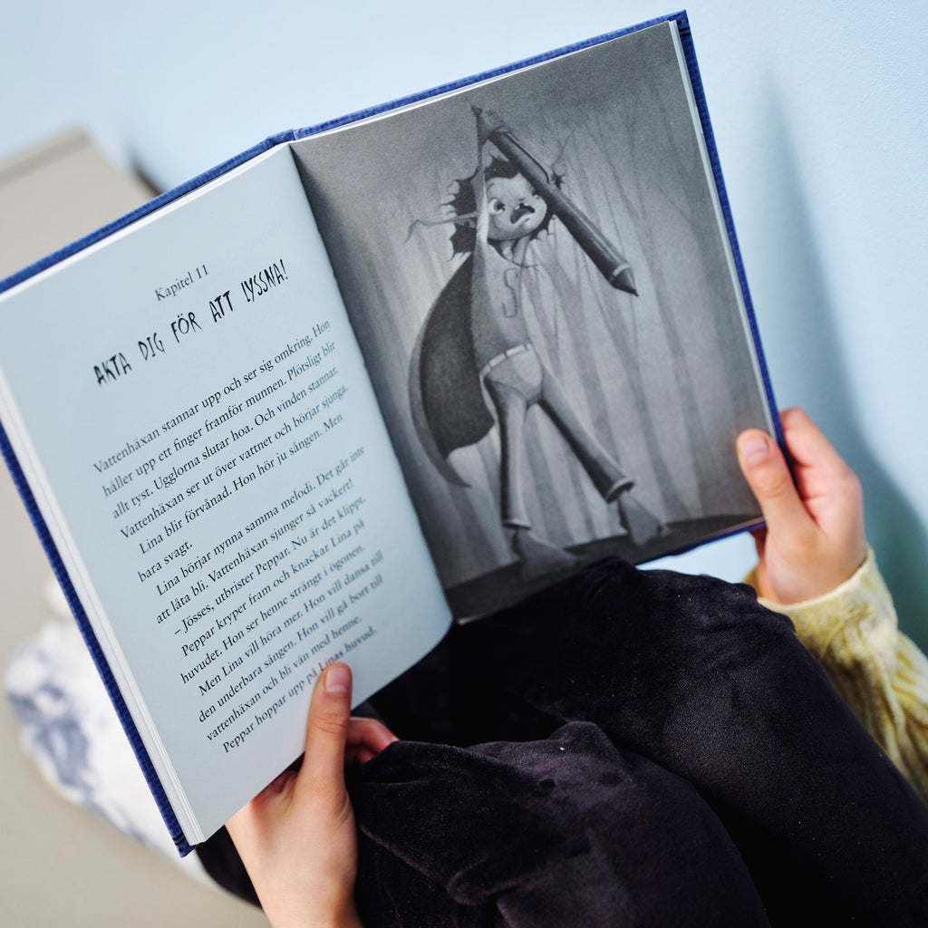 En person tittar ner på en illustration från Uppdrag: Vattenhäxan - Kapitelbok 6-9 år - OLIKA förlag - Författare: Cecilia Rihs Illustratör: Jenny Lindqvist