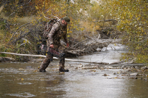 man crossing river cold weather archery hunting in Kryptek Camo