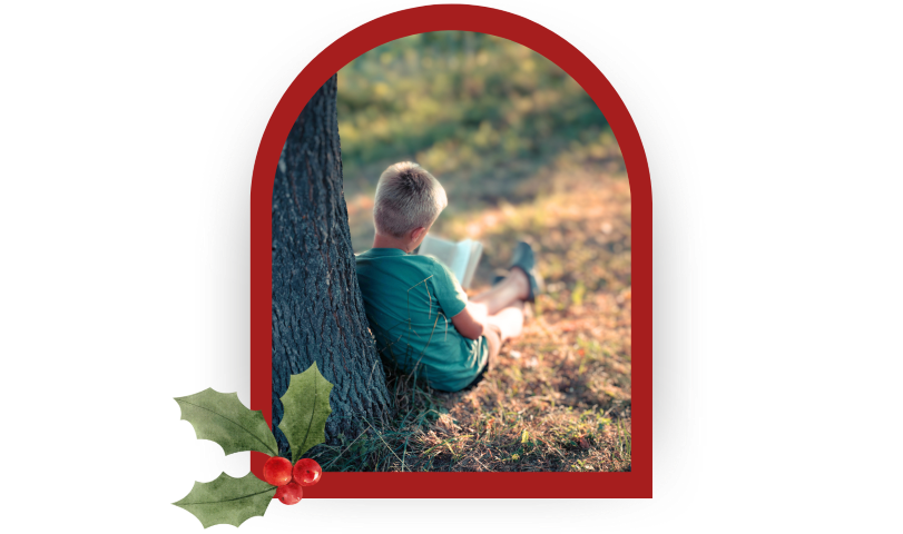 A boy reading under a shade tree with holiday graphics