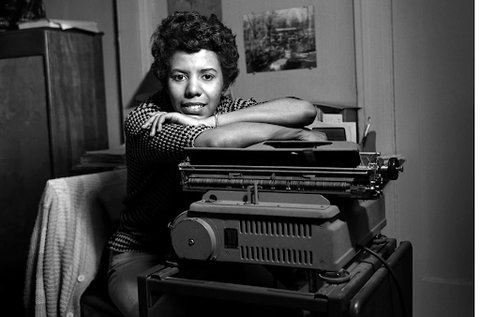 Lorraine Hansberry smiling in black in white picture while leaning over machinery