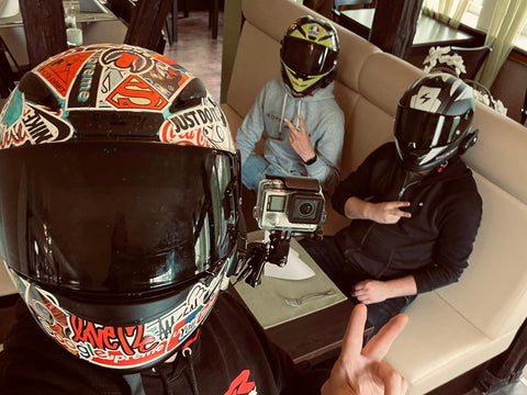 drei Motorradfahrer die in einem Restaurant mit Motorradhelmen an einem Tisch sitzen. einer der Jungs hat eine GoPro an seinem Helm und macht das Selfie