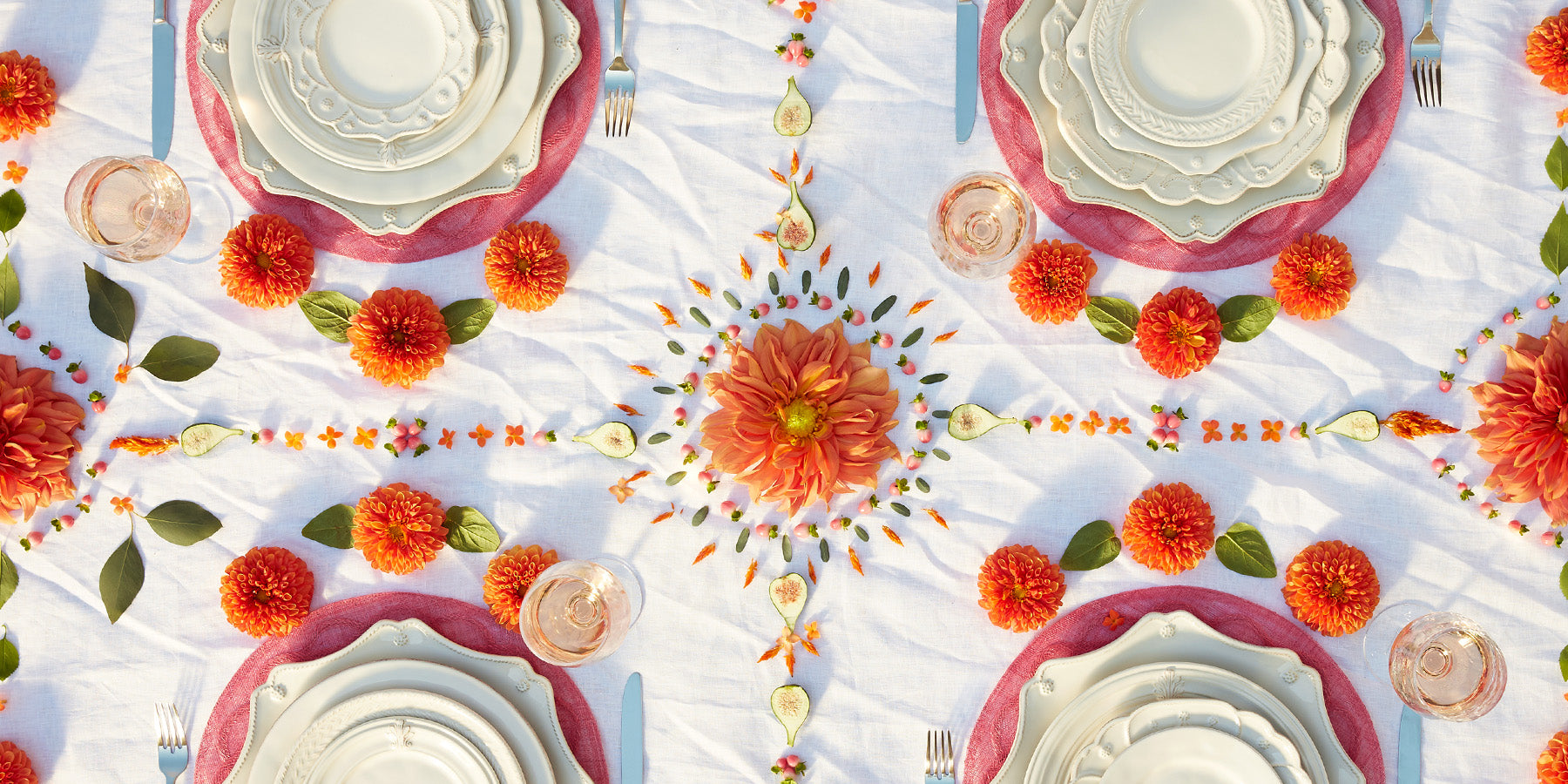 An overhead photo of white place settings on a white table cloth with orange and pink flowers.