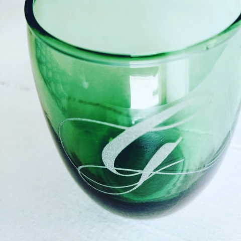 Green stemless wineglass with 'g' laser engraved on it.