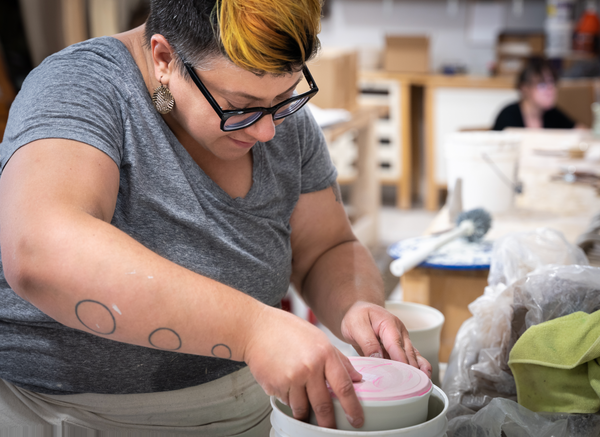 Bethany at work in her studio dipping a planter into a bucket of glaze