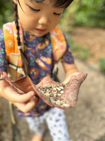 girl wearing toddler backpack and leggings showing a leaf with pebbles