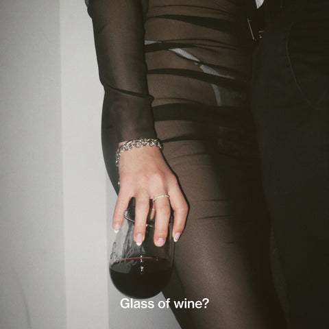 Girl in sheer dress holding a glass of red wine with french nails and a tiffany bracelet.