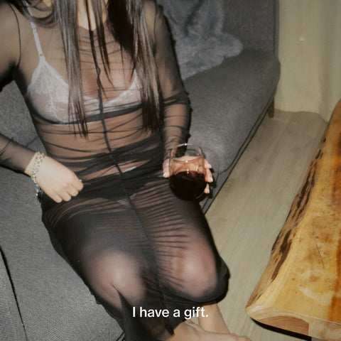 Girl with long hair in a sheer dress and white lingerie holding a glass of red wine waiting for her boyfriend