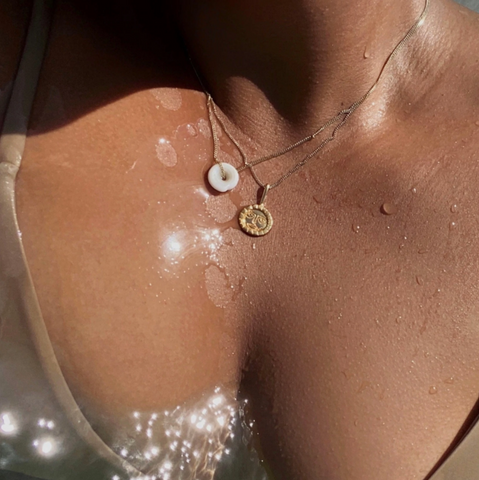 Two gold necklaces laying on tanned women's chest wearing an tan bathing suit