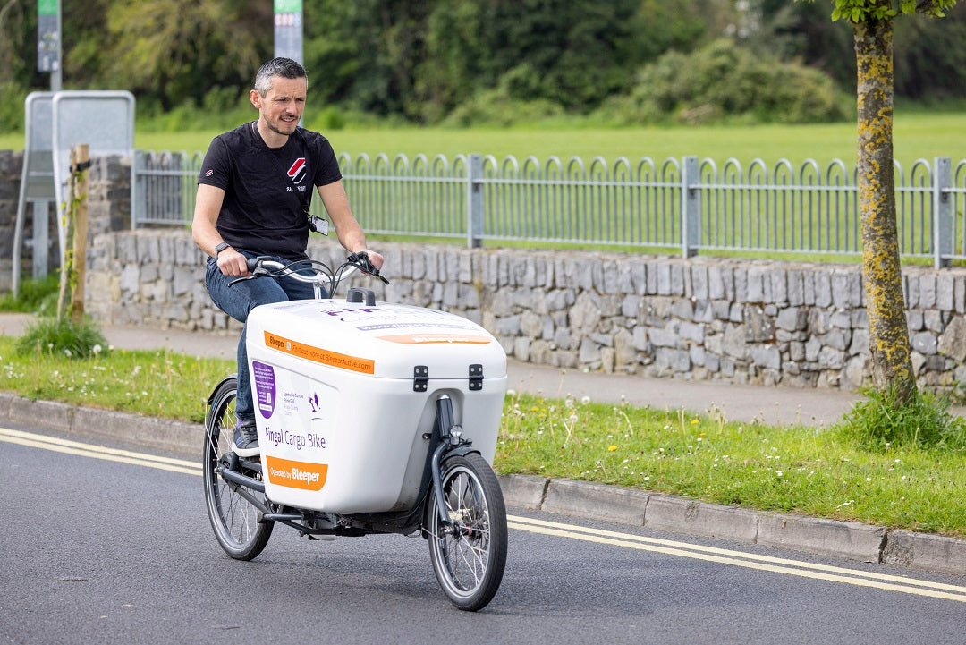 A man cycles the Fingal Cargo Bike down a street. The cargo bike is operated by Bleeper and can be hired using the Bleeper app.