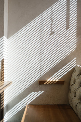 Morning sun peeking through blinds over a wooden bed, creating shadow patterns.