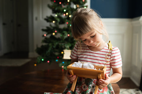 A young girl holds her Good Deeds Manger and smiles sweetly at her Baby Jesus doll.