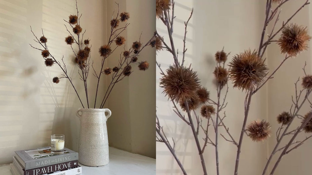 Faux gum blossom stems in a tall off white vase next to a stack of books and candle
