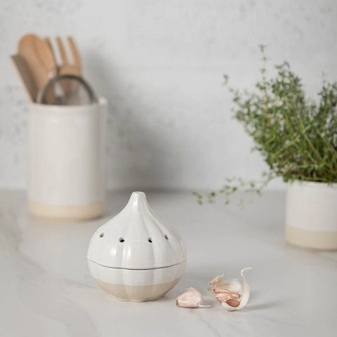 image of a stoneware garlic pot holder on a table with kitchen utensils behind