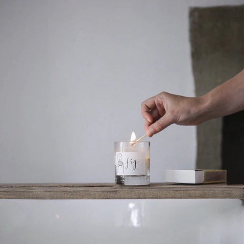 white soy candle in a glass jar lit by a match just above it