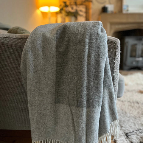 a grey and white wool throw over the arm of a sofa with soft orange lighting in the background
