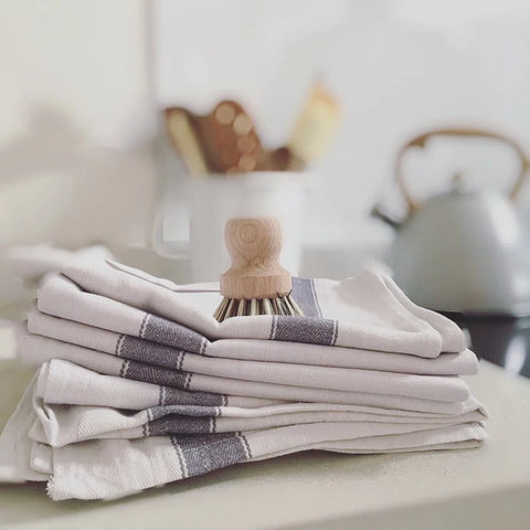 white and blue tea towels folded on top of one another with a dish brush on top