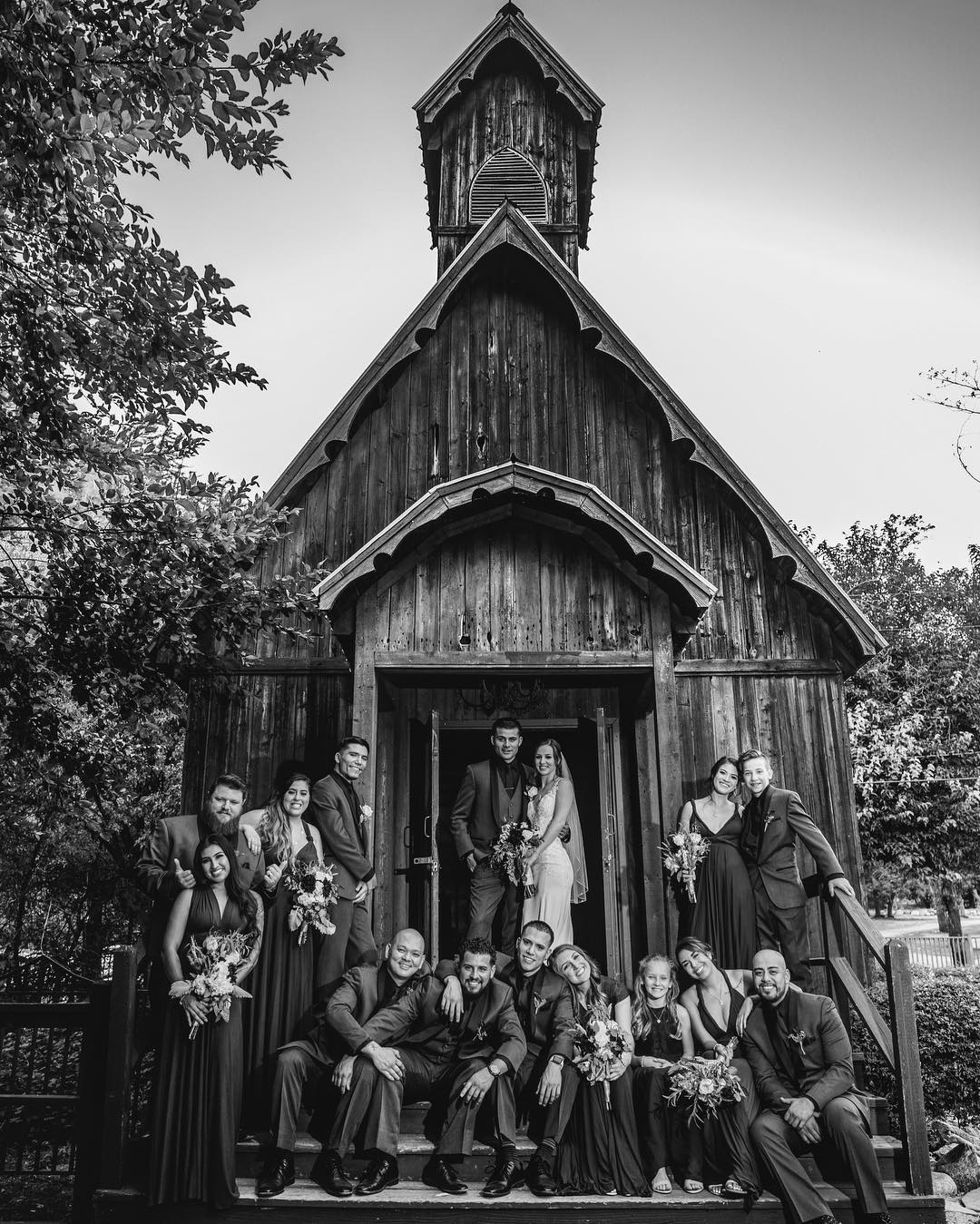 A monochrome image of the wedding party posing in front of a building 