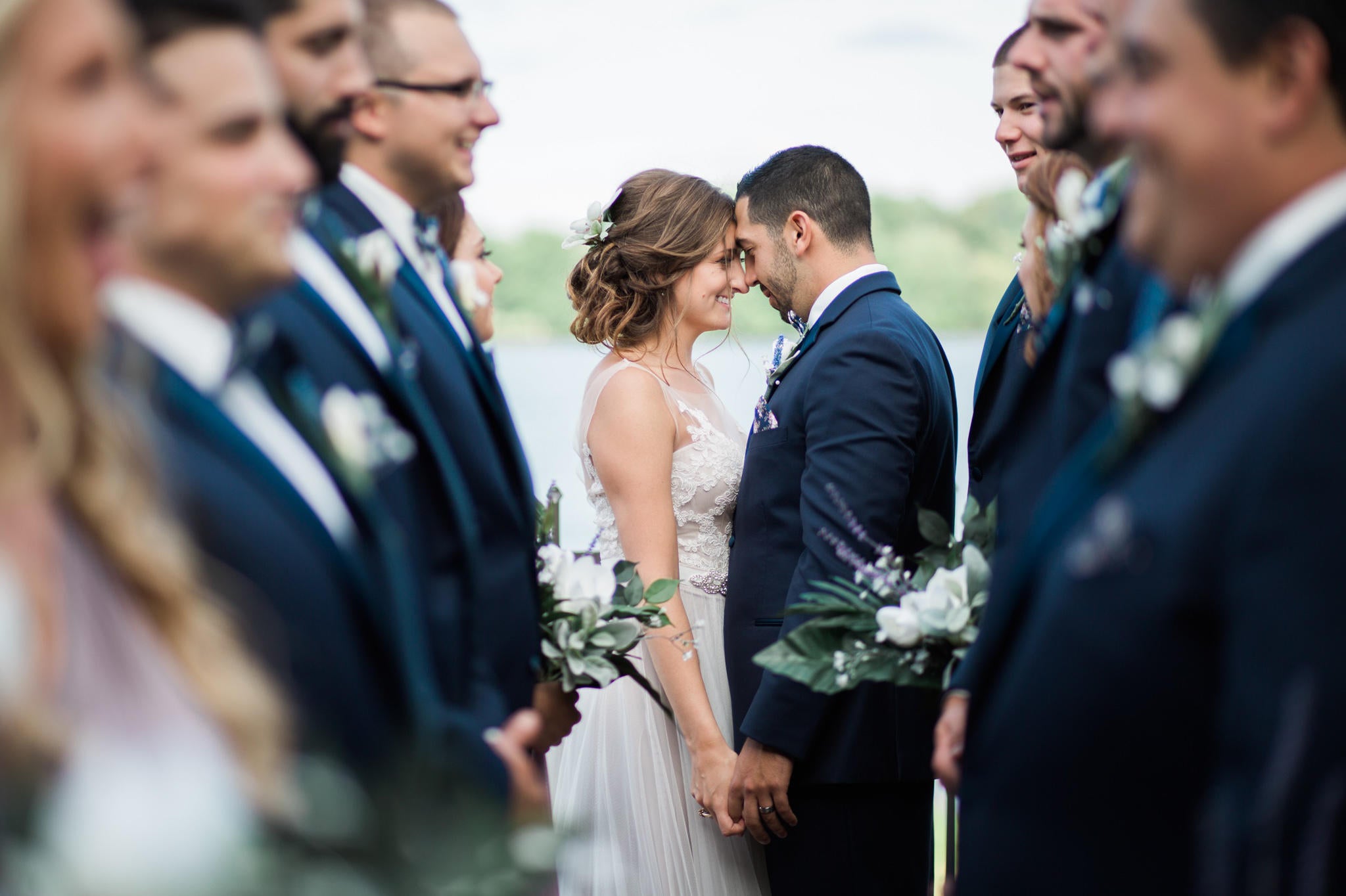 wedding couple forehead to forehead with their wedding party out of focus