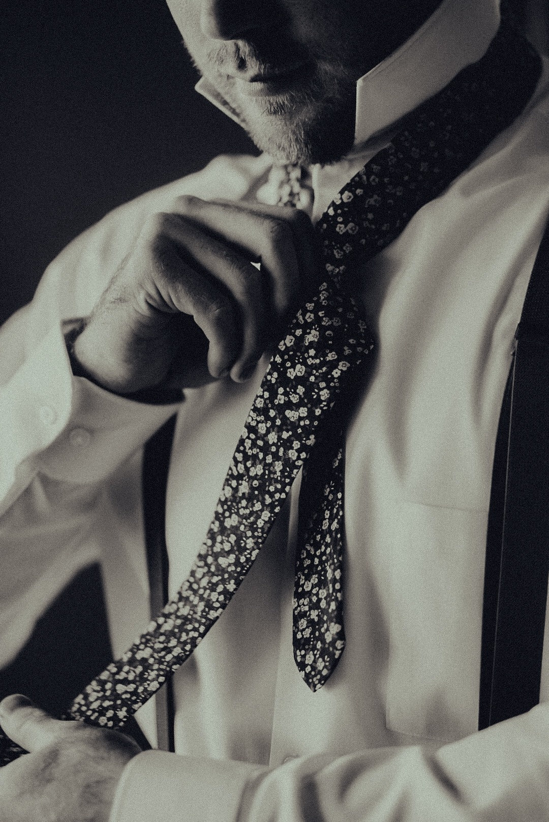 A black and white portrait of a groom adjusting his tie