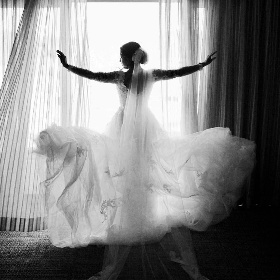 A bride standing in front of a window drawing the curtains 