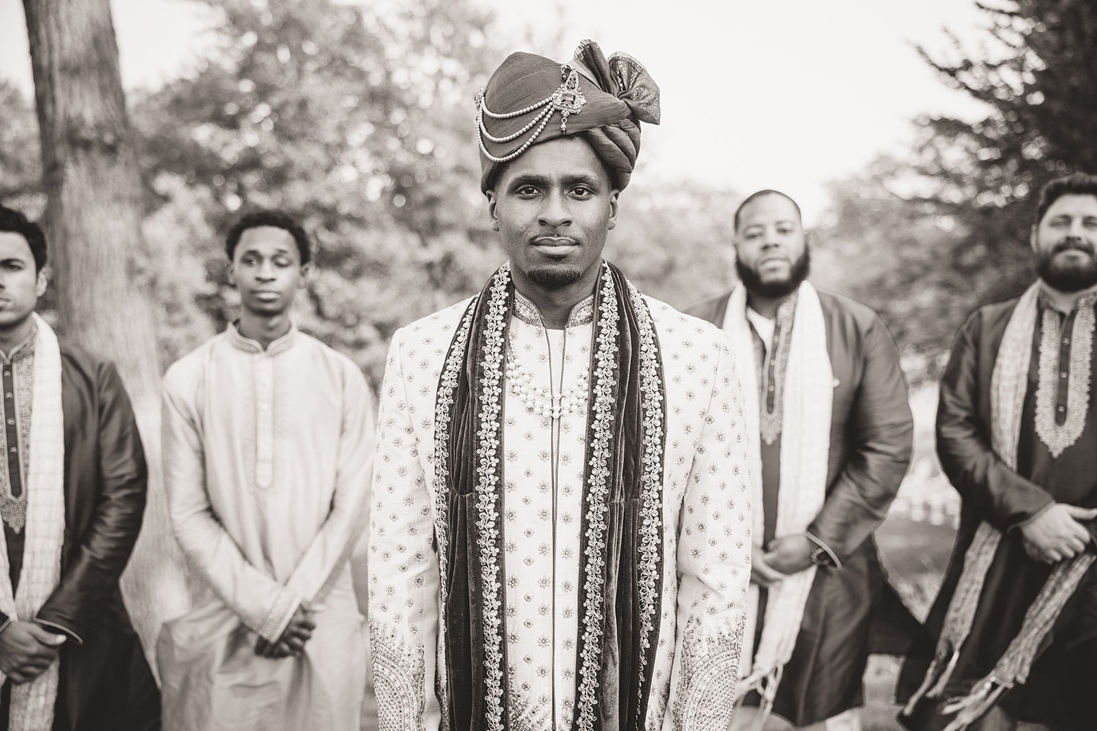 A monochrome image of a groom posing with his groomsmen with him being at the center