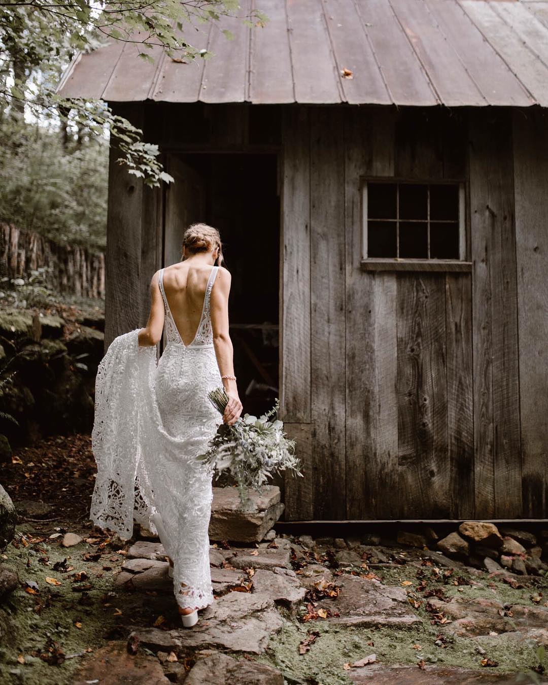 A bride holding the train of her dress as she walks towards the hut 