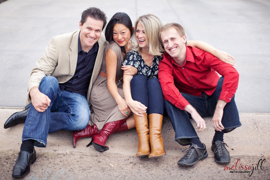 A family portrait of four while they sit at the edge of their driveway, side by side.