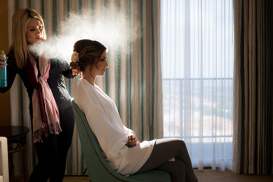 A hairstylist setting the bride's hair by spraying the hair-setting spray over her hair