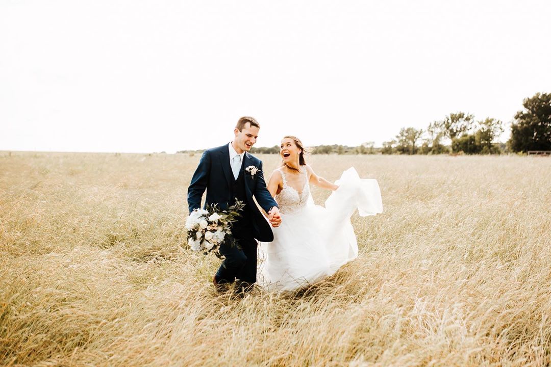 A bride and groom walking hands in hands on a field while laughing