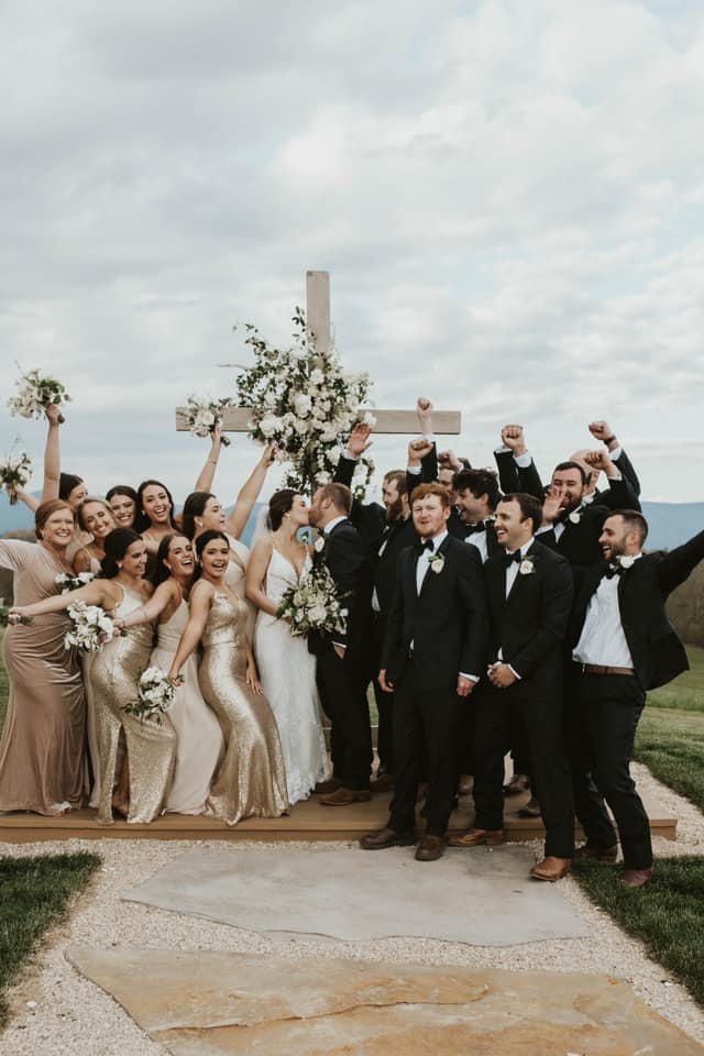 a wedding couple kissing while the wedding party is striking a fun pose in front of the wedding altar cross