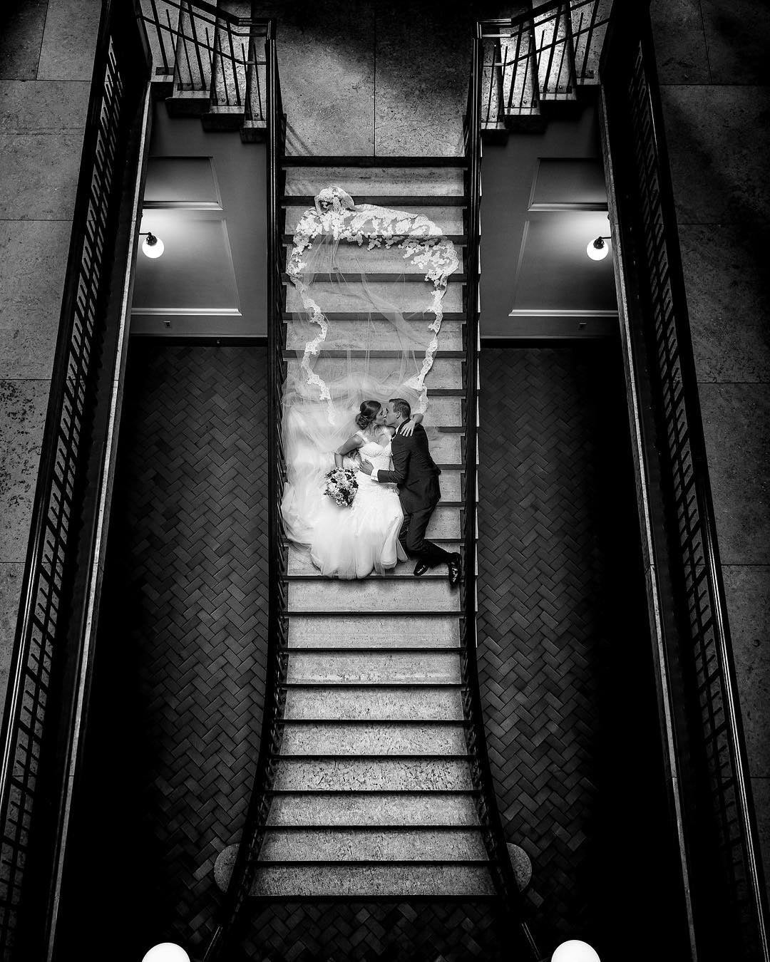 a wedding couple lying down on the stairs and kissing in their wedding attire